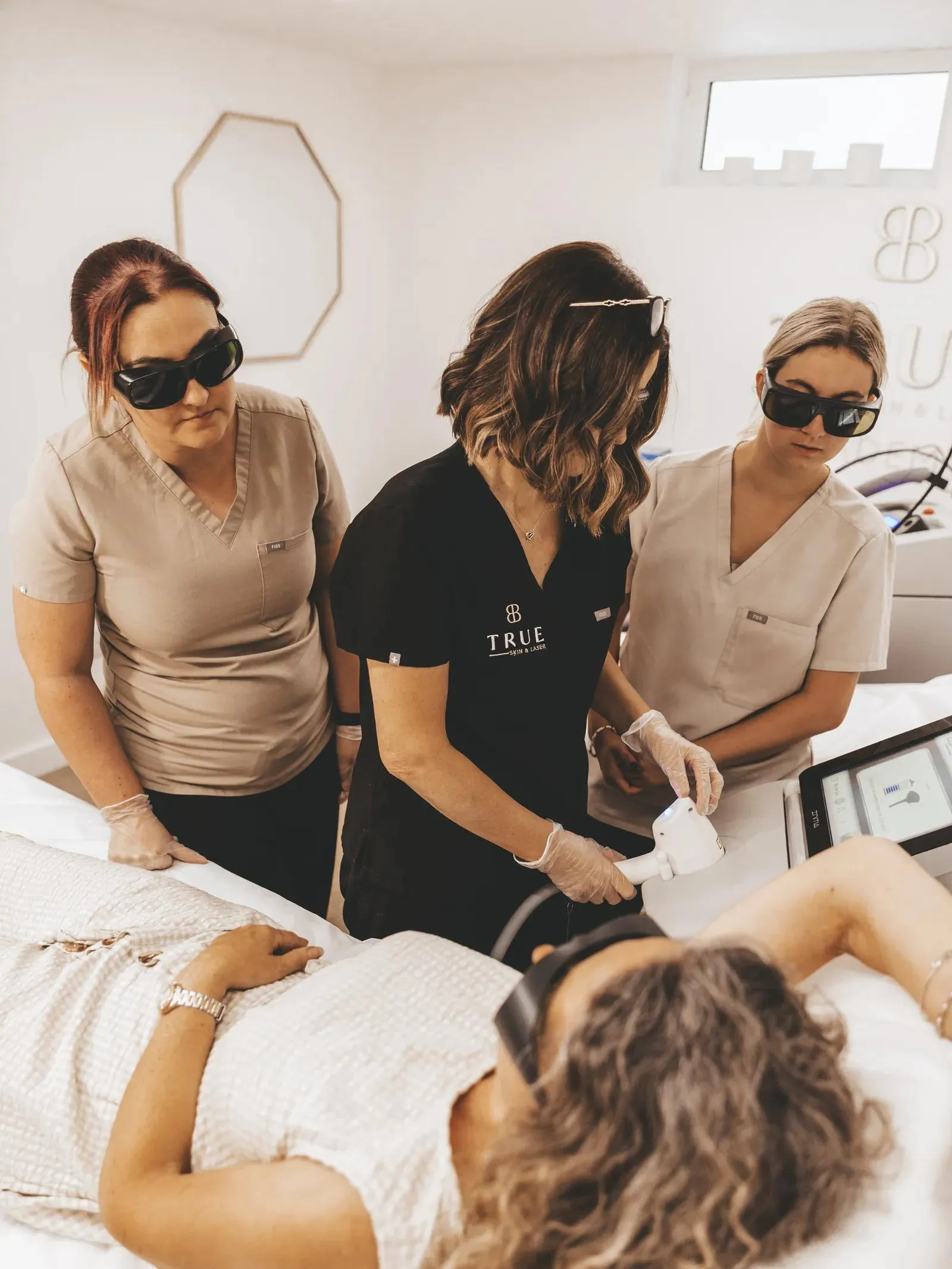 Three trainees observing a laser hair removal treatment during training at the academy