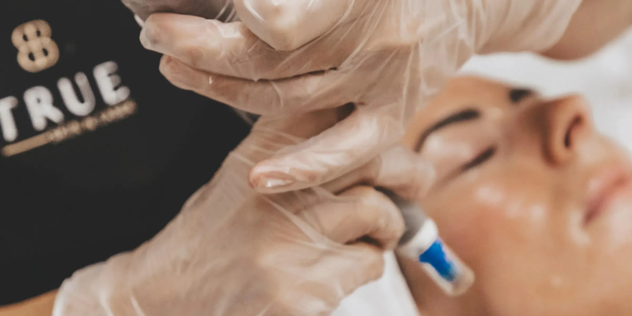Gloved hands fitting a cartridge to a microneedling pen beside a client's face