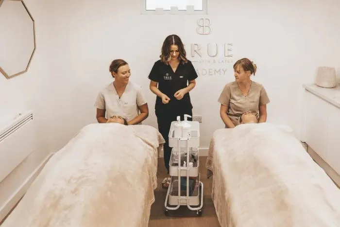 Sarah teaching two students working on clients in the academy treatment room