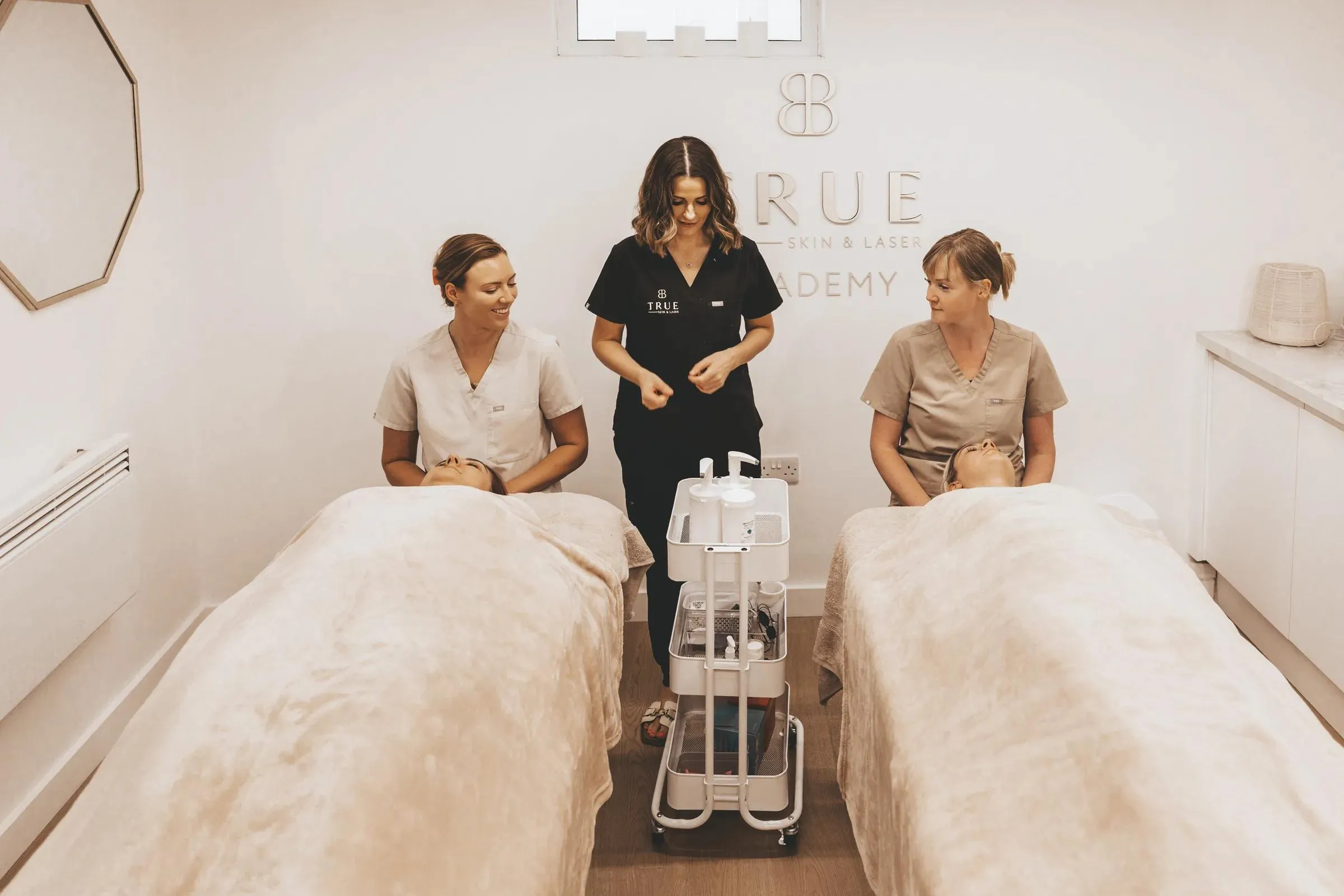 Sarah supervising two students, each treating a client on their own bed in the academy treatment room